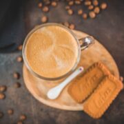 Super quick Biscoff Latte placed on small wooden plate next to two Biscoff cookies.