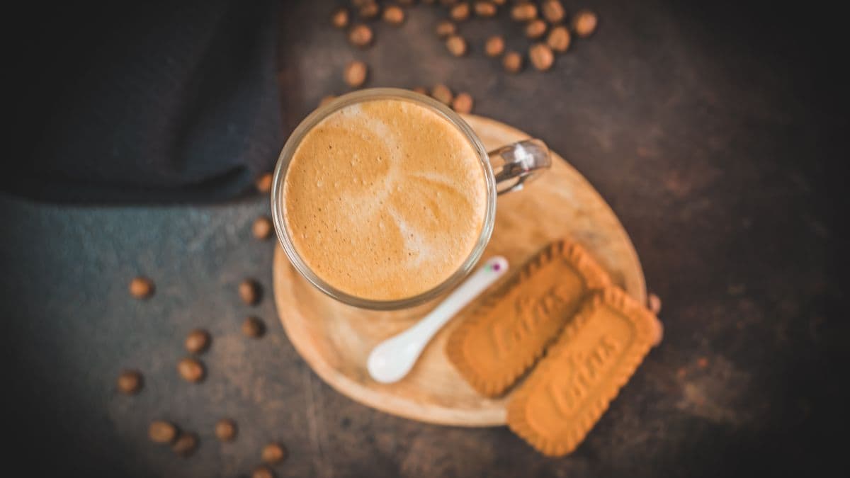 Super quick Biscoff Latte placed on small wooden plate next to two Biscoff cookies.