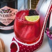 Chambord gin and tonic playfully placed in a red and white polka dot high heel. Garnished with a lime wedge and a black berry.