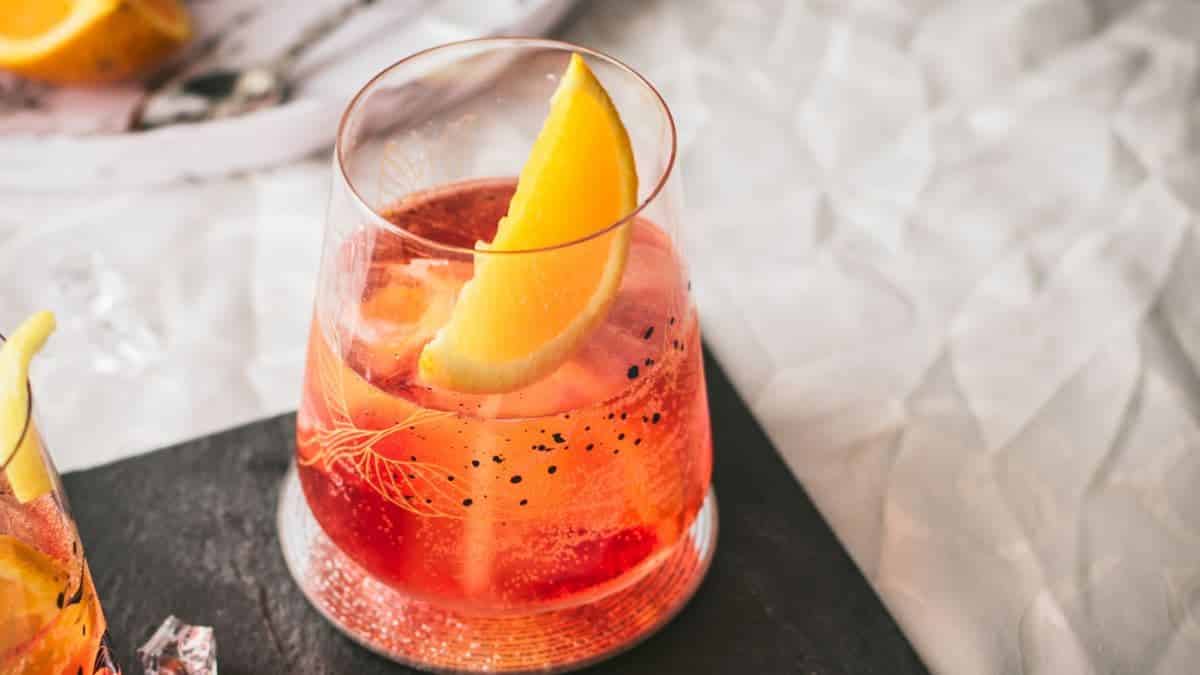 Gorgeous Americano cocktail garnished with an orange wedge and placed on a black slate plate.