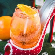 Aperol spritz with white wine instead of prosecco playfully served in a red and white polka dot high heel. Garnished with n orange slice.