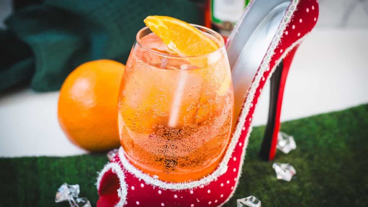 Aperol spritz with white wine instead of prosecco playfully served in a red and white polka dot high heel. Garnished with n orange slice.