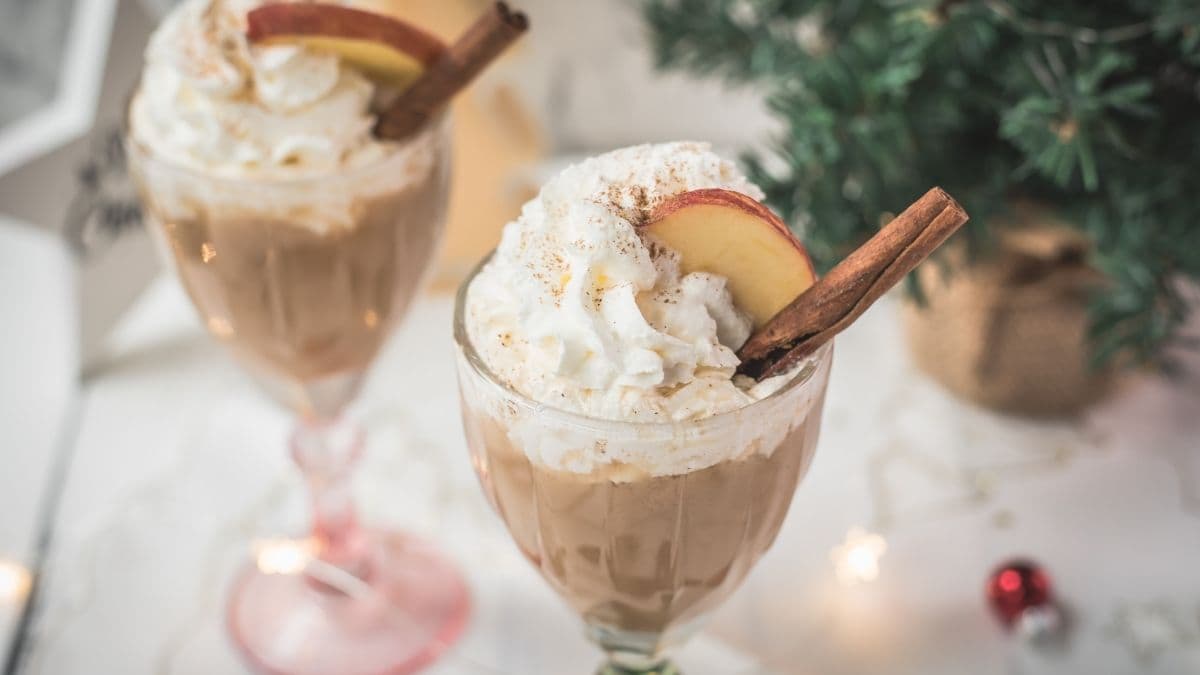 Decadent apple cider eggnog, garnished with a cinnamon stick, whipped cream, and apple slices.