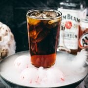 Bourbon and root beer Halloween cocktail with bourbon and root beer bottles in the background.