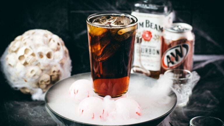 Bourbon and root beer Halloween cocktail with bourbon and root beer bottles in the background.