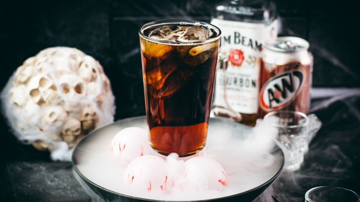 Bourbon and root beer Halloween cocktail with bourbon and root beer bottles in the background.