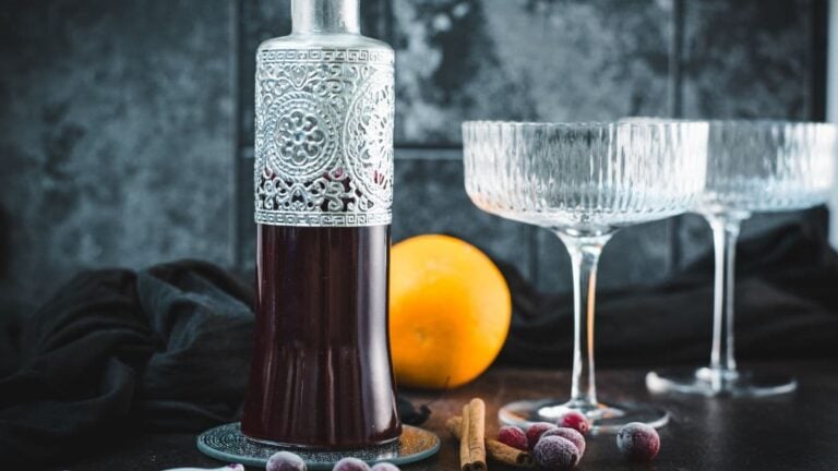 Homemade cranberry simple syrup in a decorative glass bottle with frozen cranberries, cinnamon, and orange