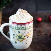 Scrumptious eggnog latte with whipped cream topping and dusted with cinnamon, served in gorgeous Christmassy mug.