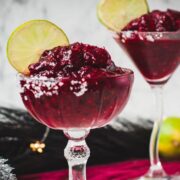 Magnificent frozen mixed berry margarita, served in cocktail glasses, garnished with a lime slice. With a vibrant dark red color. What an eye-catcher!