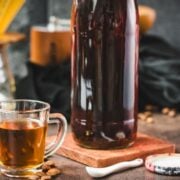 Amazing coffee syrup, in small glass next to a preserving bottle filled with coffee syrup, placed on brown ground next to coffee beans.