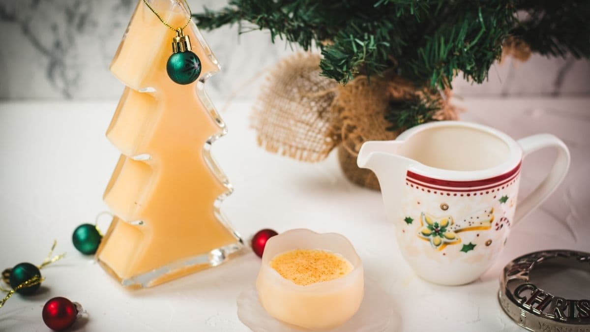 Delicious eggnog in a small icy bowl next to a Christmas tree shaped bottle, filled with eggnog.