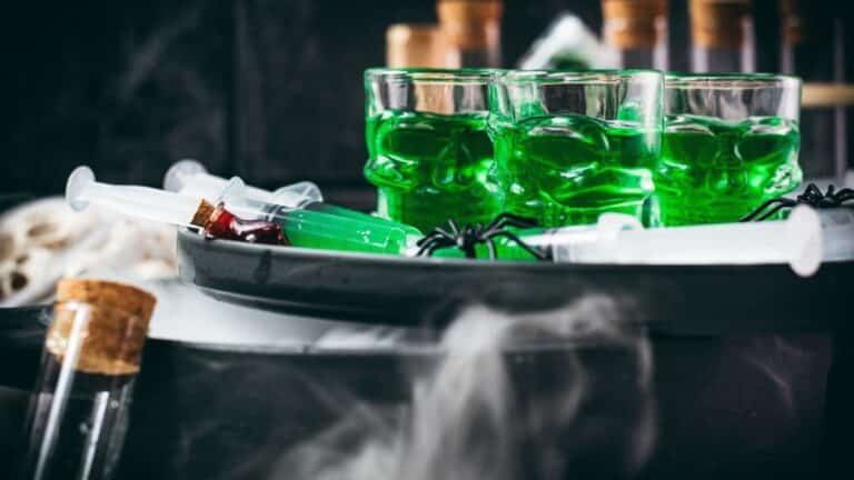 Toxic green Halloween Jello shot syringes and skull-shaped glasses with swirling dry ice smoke