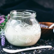 Gorgeous preserving glass, filled with homemade lavender coffee creamer. Placed on dark ground covered with dried lavender buds.