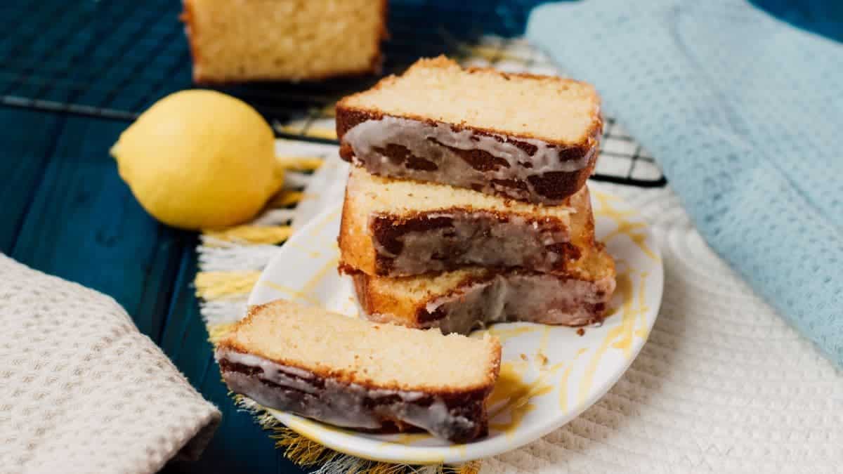 Sliced and stacked lemon loaf cake slices, placed on white and yellow plate, next to a lemon.