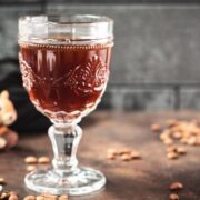 Gorgeous glass filled with maple syrup coffee, placed on dark brown ground, next to a tiny little squirrel figure.