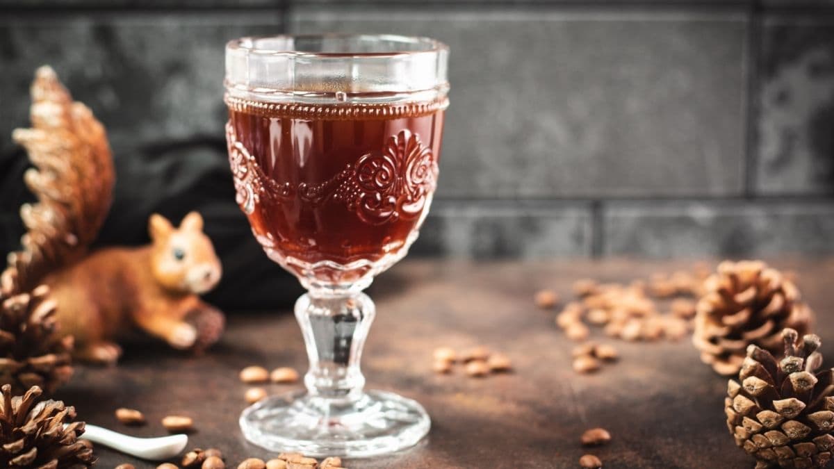 Gorgeous glass filled with maple syrup coffee, placed on dark brown ground, next to a tiny little squirrel figure.