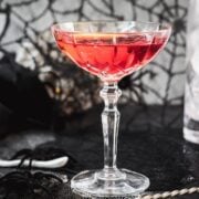 Cocktail Glass filled with a stunning red old pal cocktail, garnished with a lemon zest, and placed on spider web covered ground.