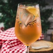 Delicious Zirben Spritzer served in white wine glass. Placed on wooden ground, next to a flask of Zirben Schnapps.