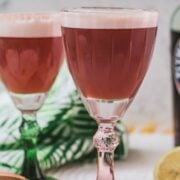 Divine ruby fizz cocktail, placed on mirrored coaster and served in a red and a green glass.