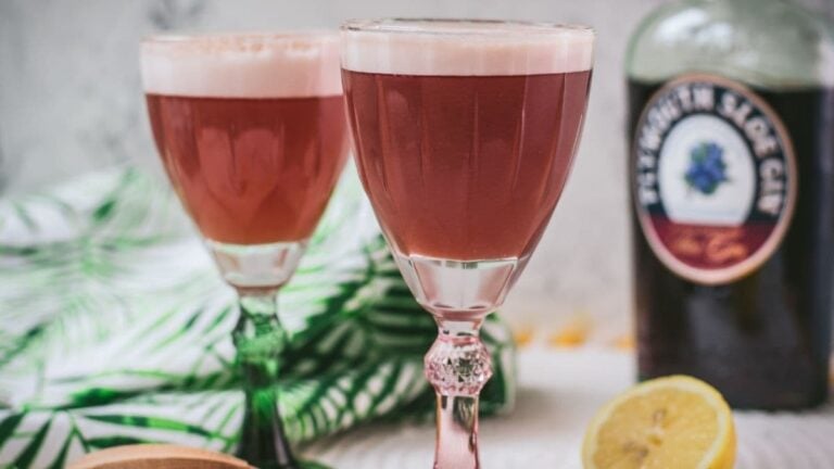 Divine ruby fizz cocktail, placed on mirrored coaster and served in a red and a green glass.