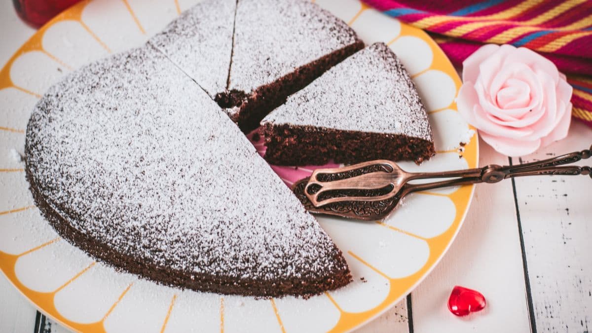 Delicious heart-shaped chocolate cake, dusted with powdered sugar. Ideal for Valentine's day! Placed on yellow-white serving plate.