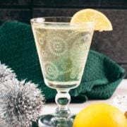 Glass with beautiful flower engraving, filled with delicious White Vermouth Blondie cocktail. Garnished with a lemon wedge.