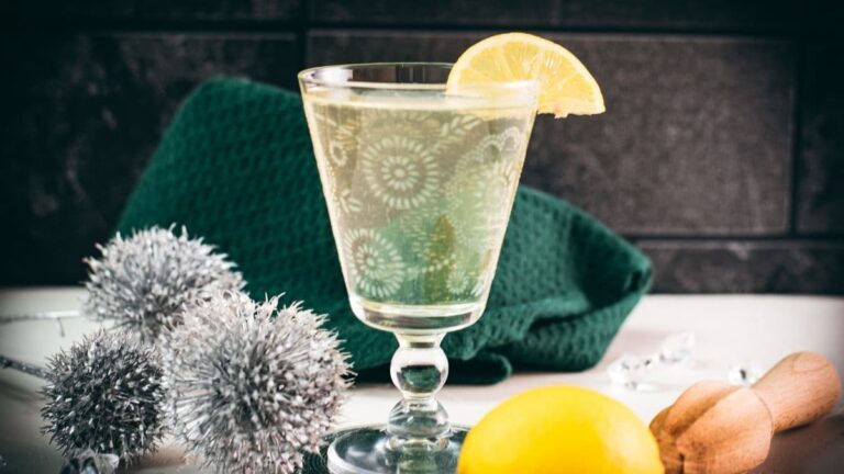 Glass with beautiful flower engraving, filled with delicious White Vermouth Blondie cocktail. Garnished with a lemon wedge.